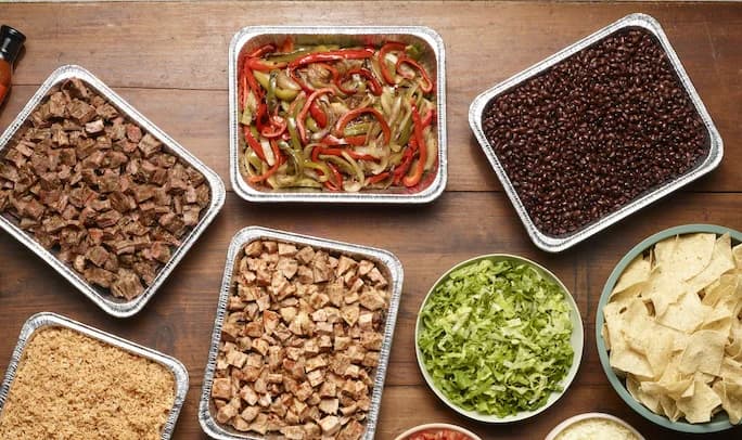 Fajita catering spread with steak, chicken, peppers and onions, black beans, rice, lettuce and tortilla chips