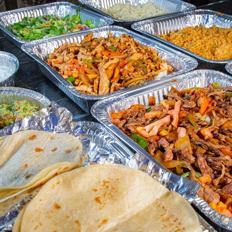 Fajita catering spread with steak, chicken, peppers and onions, black beans, rice, lettuce and tortilla chips
